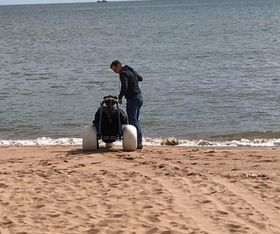 Parent and child using the hippocampe chair at the water's edge on Balmedie beach
